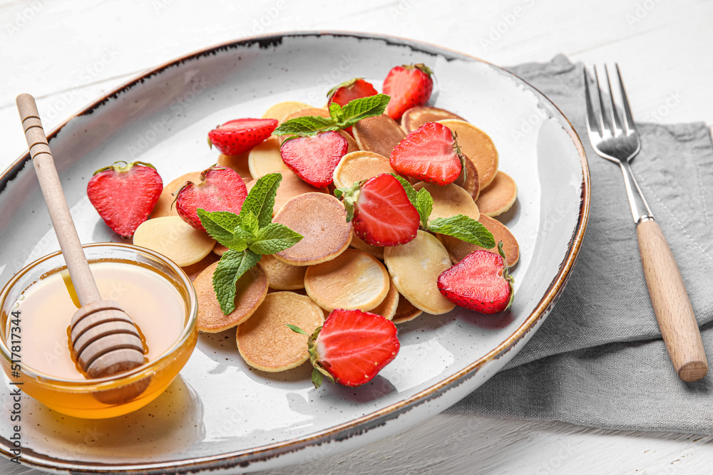 Plate with mini pancakes, strawberry and bowl of honey on table