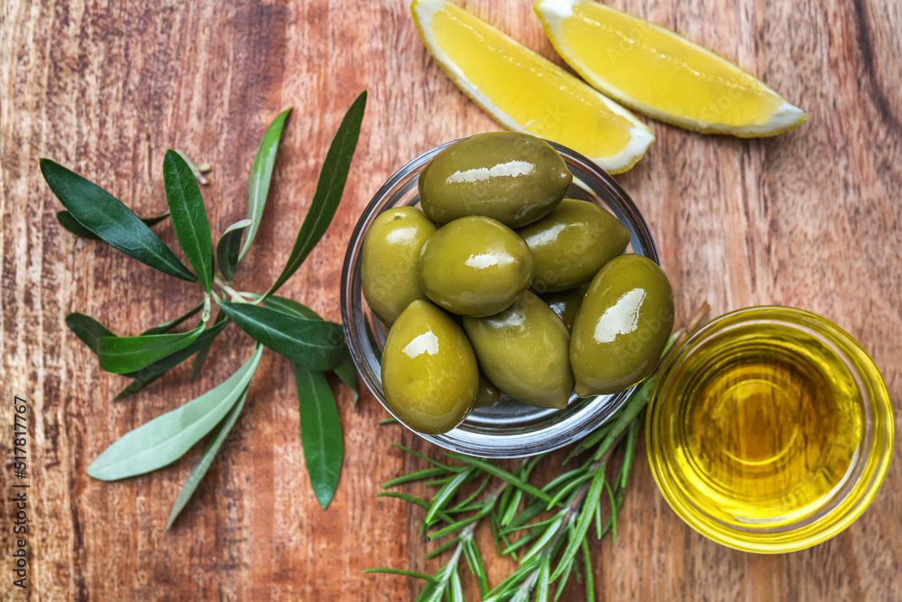 Bowls of tasty green olives, oil and lemon slices on wooden background