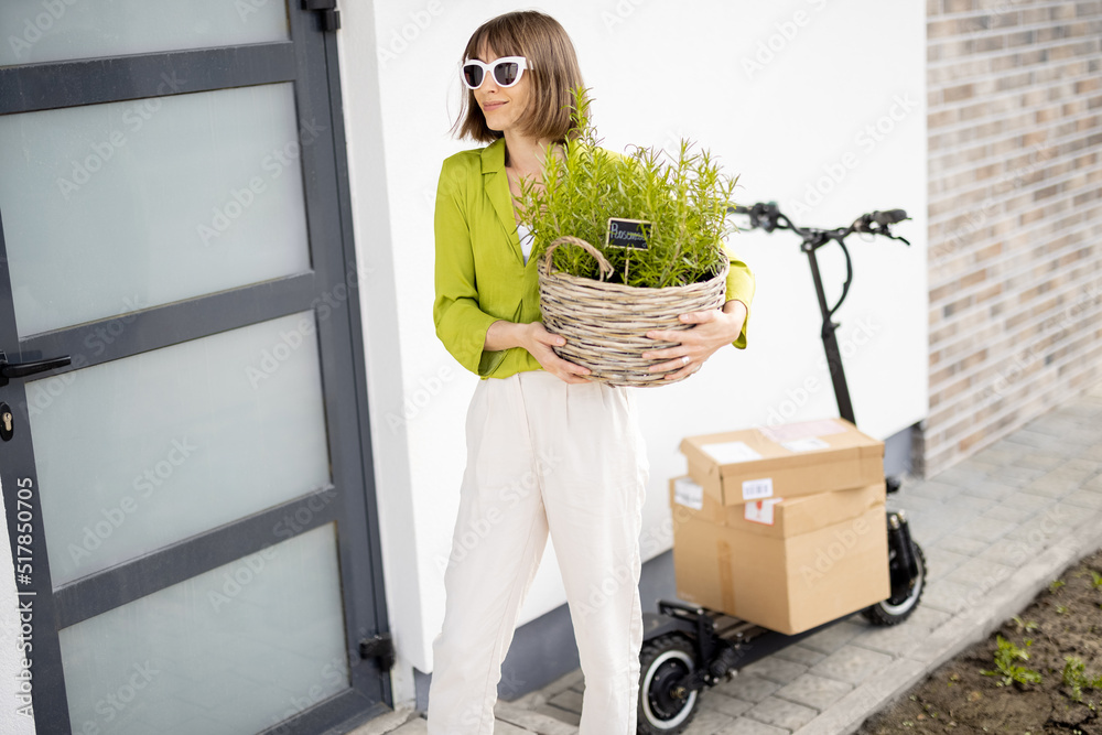 Young stylish woman carrying basket with rosemary while coming home by electric scooter. Concept of 