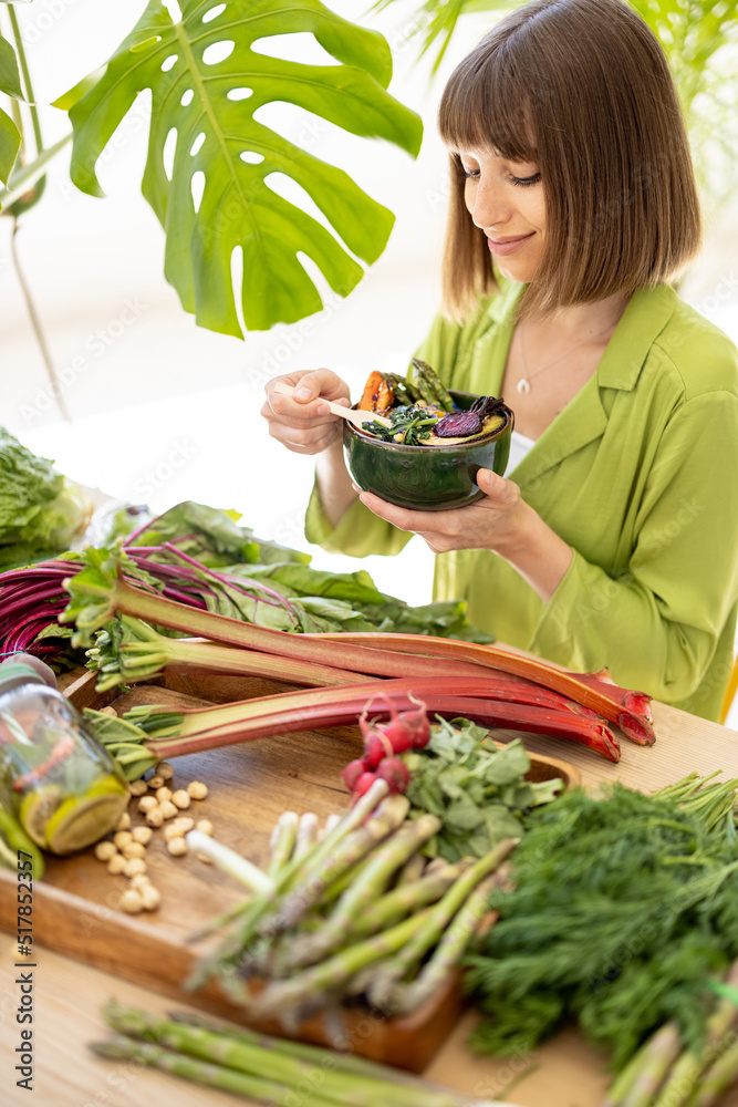 年轻开朗的女人坐在装满新鲜蔬菜和水果的桌子旁吃素食碗