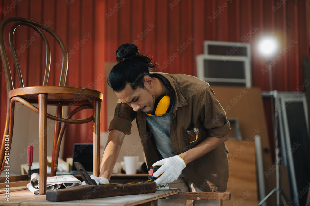 亚洲青年木匠在木工工作台上用卷尺测量椅子