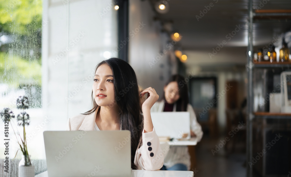 一名亚洲女子在餐厅里使用笔记本电脑，看着外面梦见什么