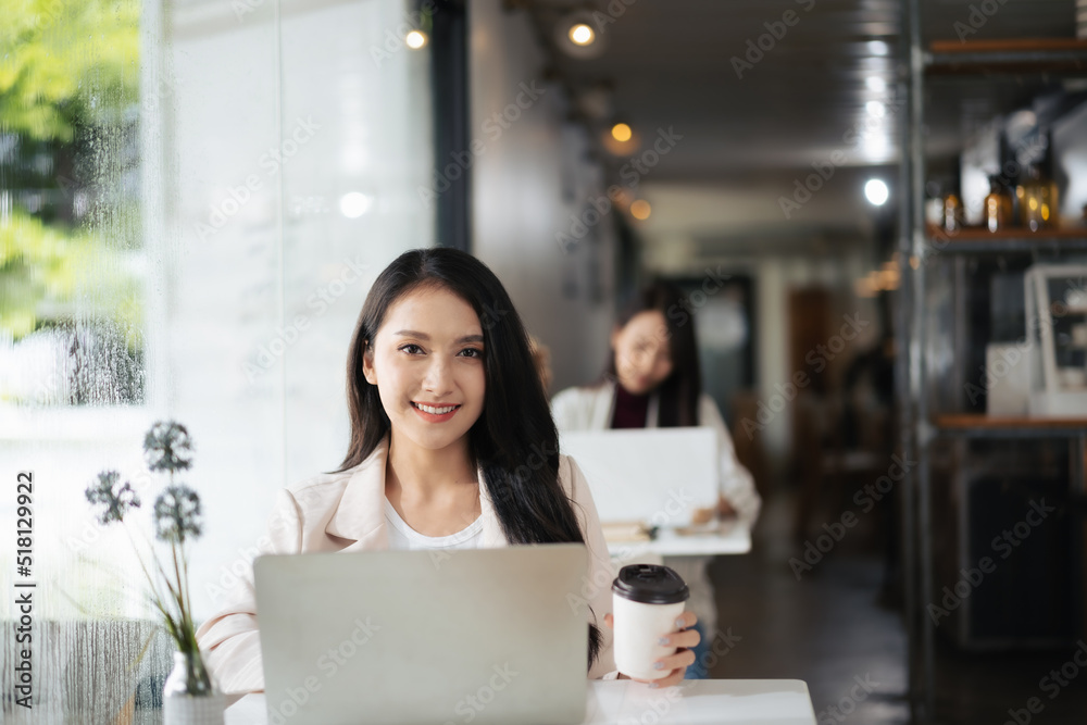 一位年轻的亚洲女性在咖啡店里用笔记本电脑看着相机。