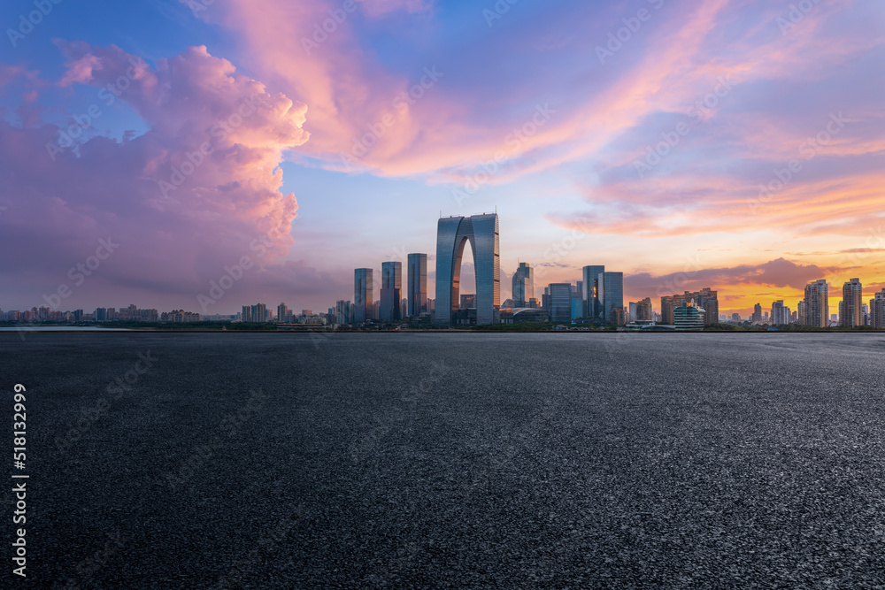 Asphalt road and city skyline with modern commercial building at sunset in Suzhou, China.