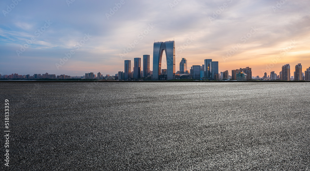 Asphalt road and city skyline with modern commercial building at sunset in Suzhou, China.