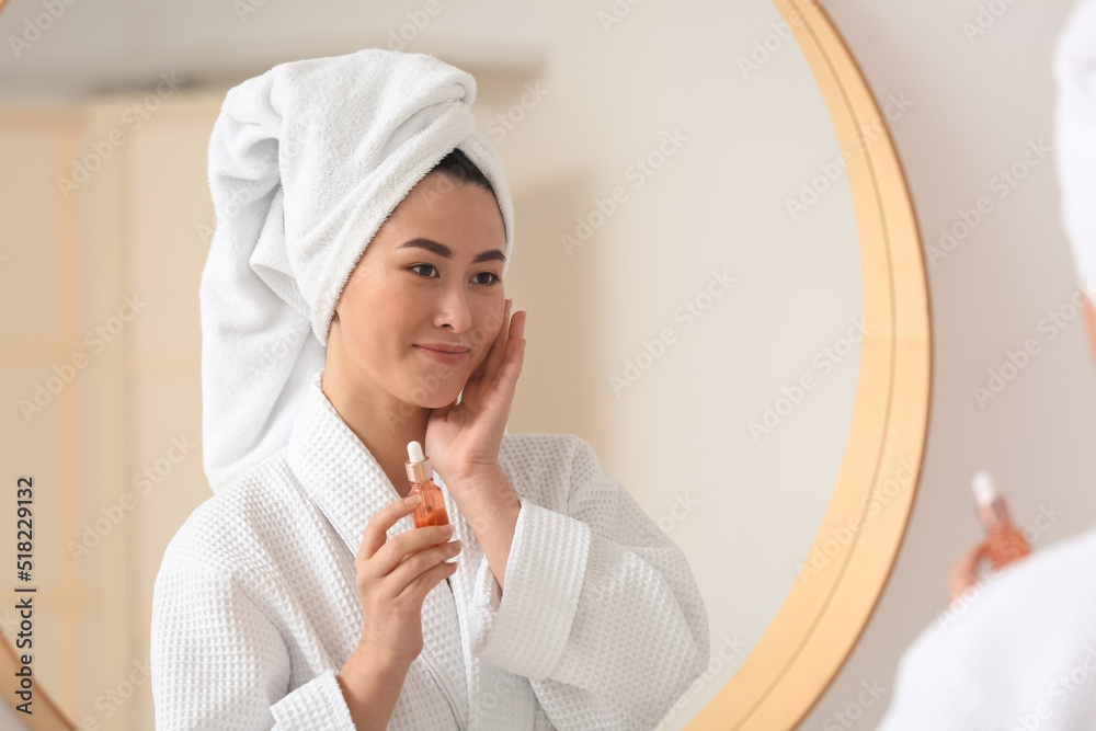 Young Asian woman using cosmetic serum in bathroom