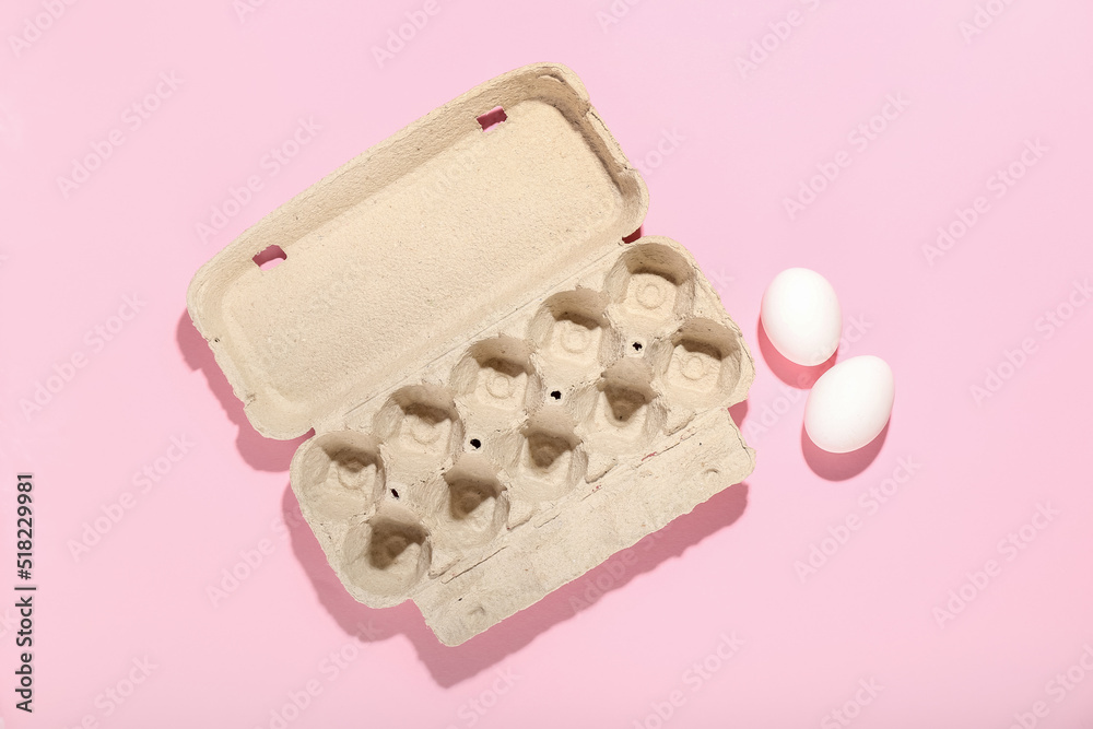 Cardboard holder with chicken eggs on pink background