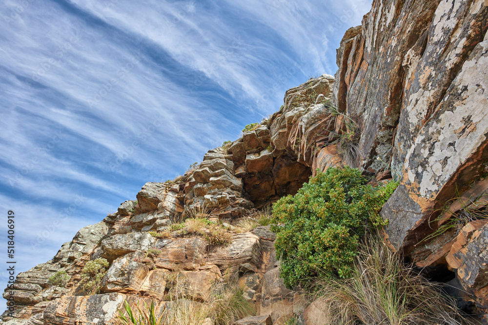 Copy space on a rocky mountain with plants and shrubs growing against a cloudy sky background. Rugge