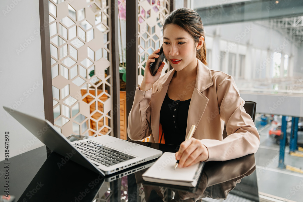 Business asian woman Talking on the phone and using a laptop with a smile while sitting at office.