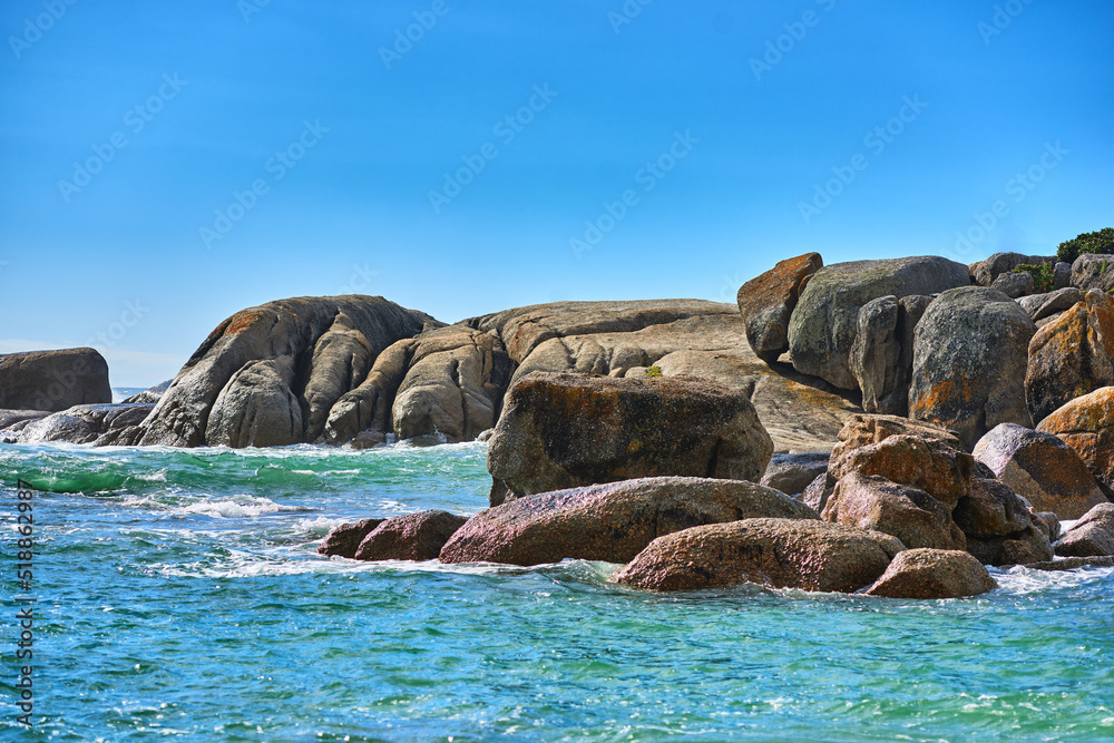 Boulders or big rocks in a calm ocean against a clear blue sky background with copy space. Beautiful