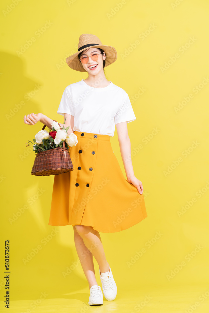 Full length photo of young Asian woman holding flower on yellow background