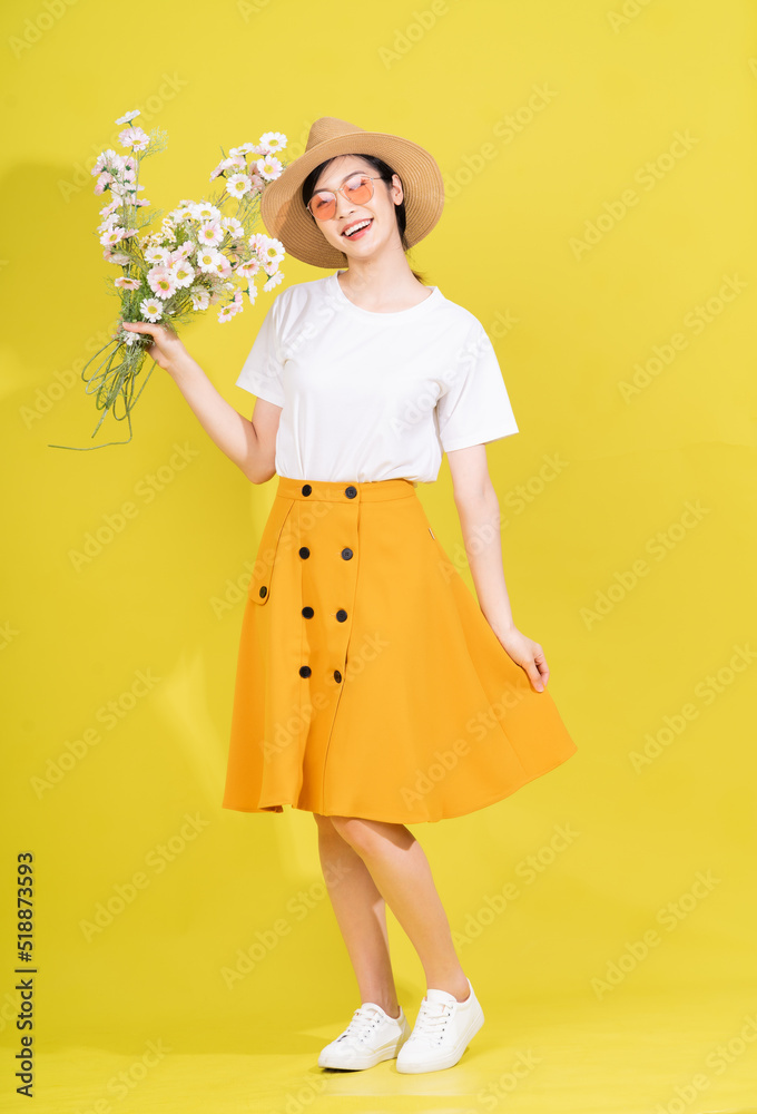 Full length photo of young Asian woman holding flower on yellow background