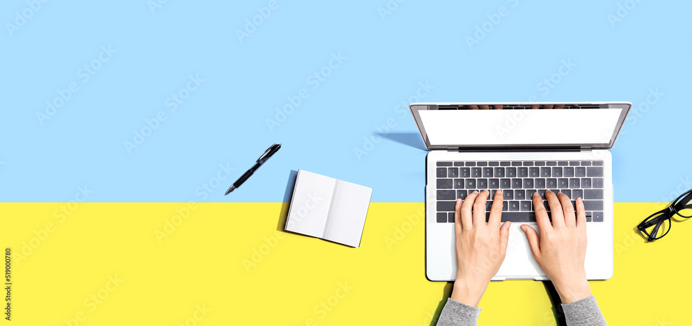 Person using a laptop computer with a notebook and eyeglasses - Flat lay