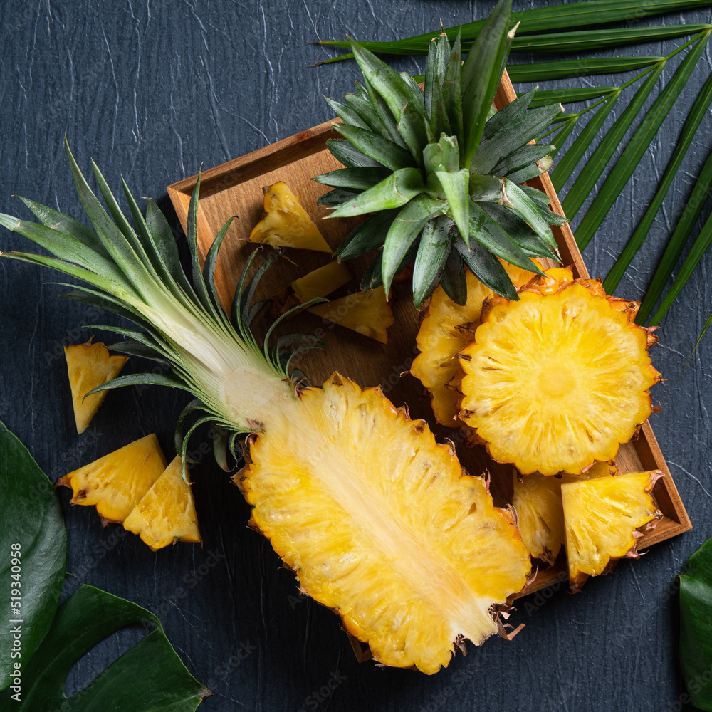 Fresh cut pineapple with tropical leaves on dark blue background.