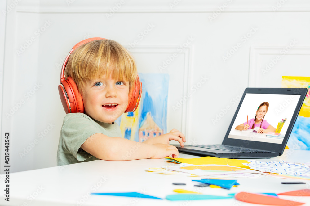 Smiling blond boy in headphones with laptop for remote education