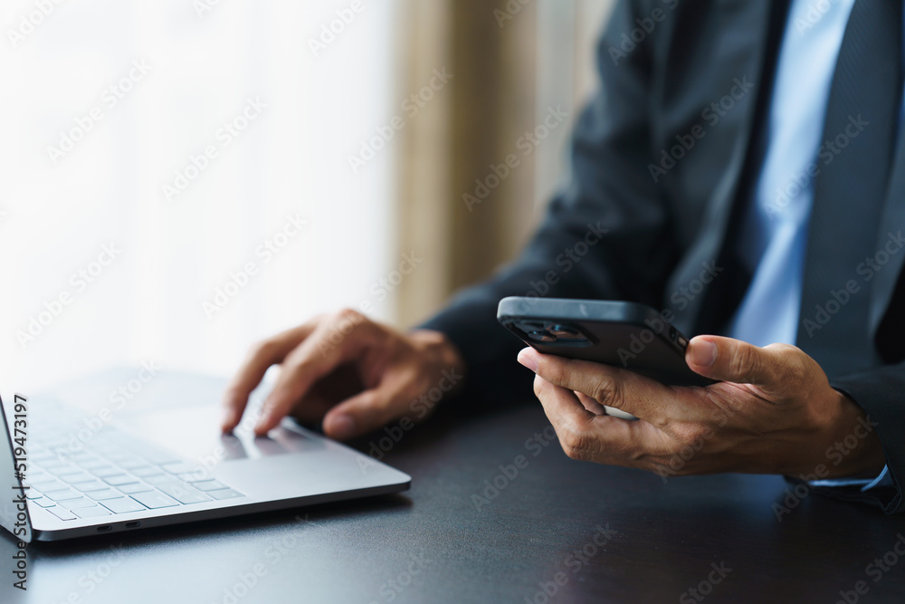 Close up businessman using a smartphone and a laptop while working from home.