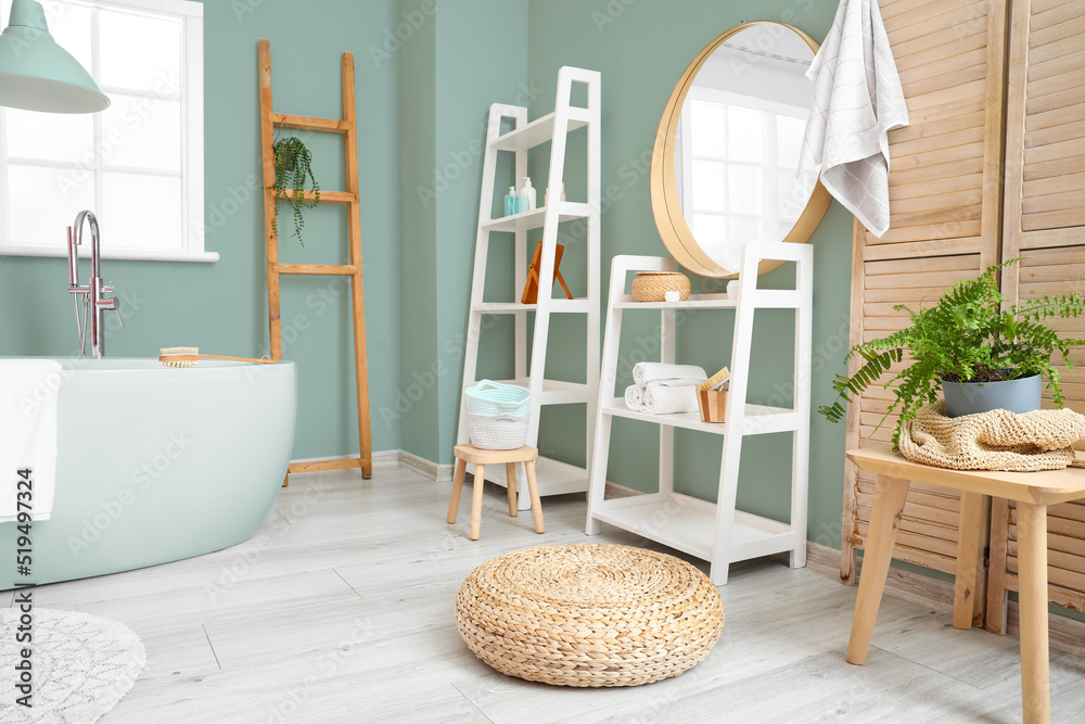 Interior of light bathroom with shelving units, bathtub and mirror