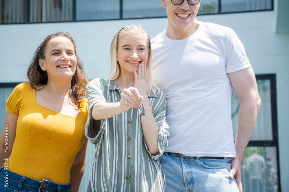 Happy family holding keys in front of their new home after buying real estate.