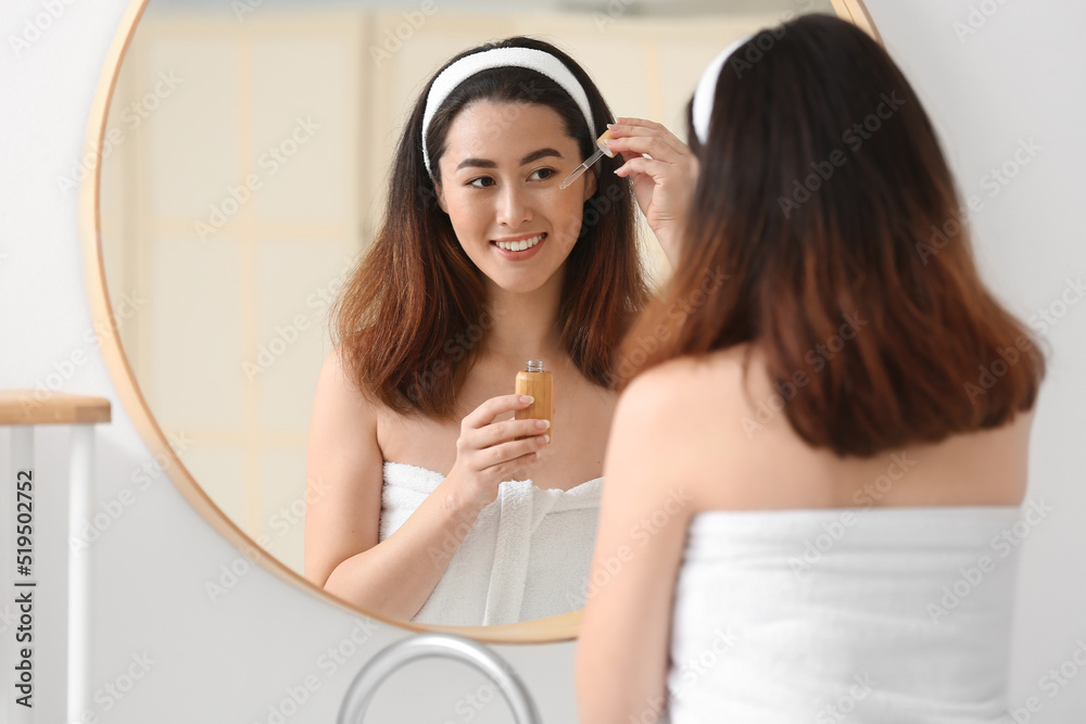 Young Asian woman using cosmetic serum in bathroom