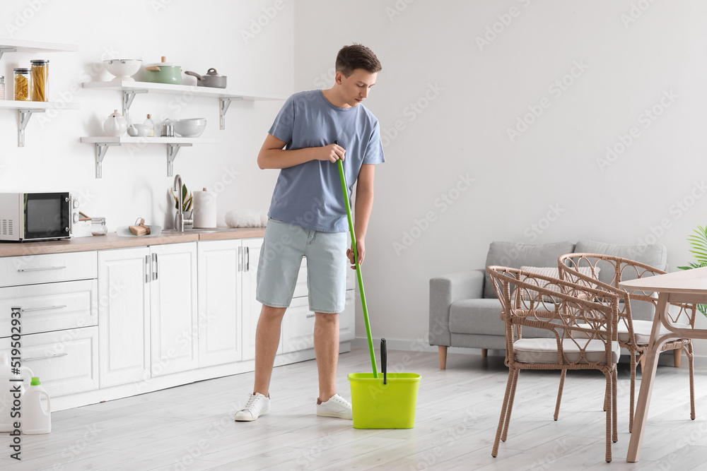 Handsome young man mopping floor in modern kitchen