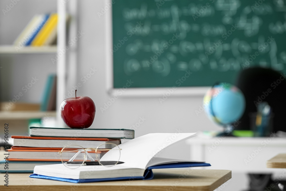 Red apple with school books and eyeglasses on table in classroom