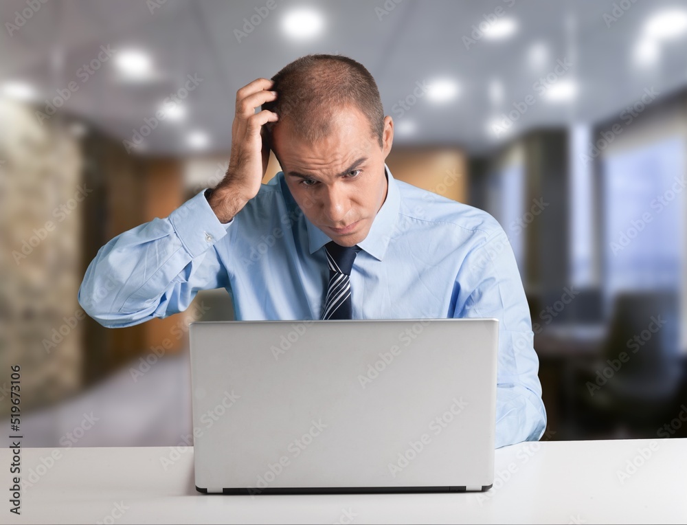 Young businessman using computer in office, thinking. Happy middle aged man, entrepreneur working on