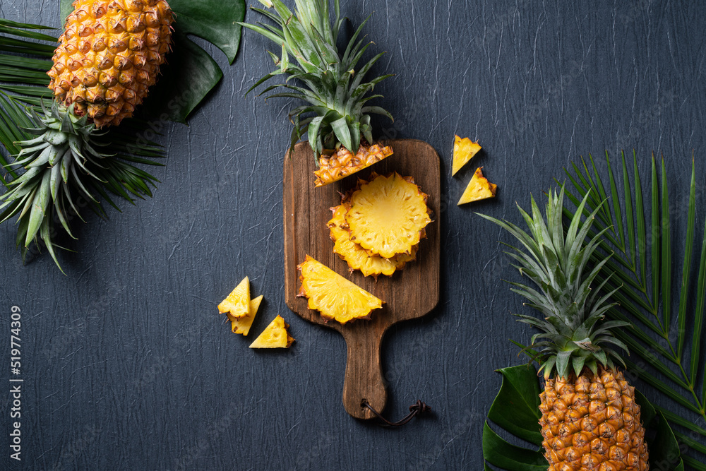 Fresh cut pineapple with tropical leaves on dark blue background.