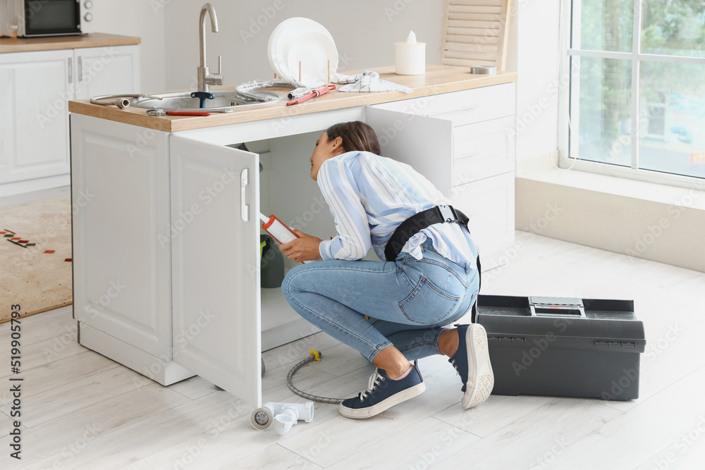 Female plumber fixing sink in kitchen