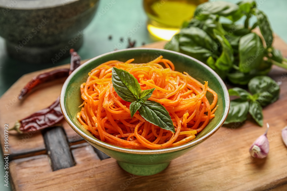 Bowl with spicy carrot salad on wooden board, closeup