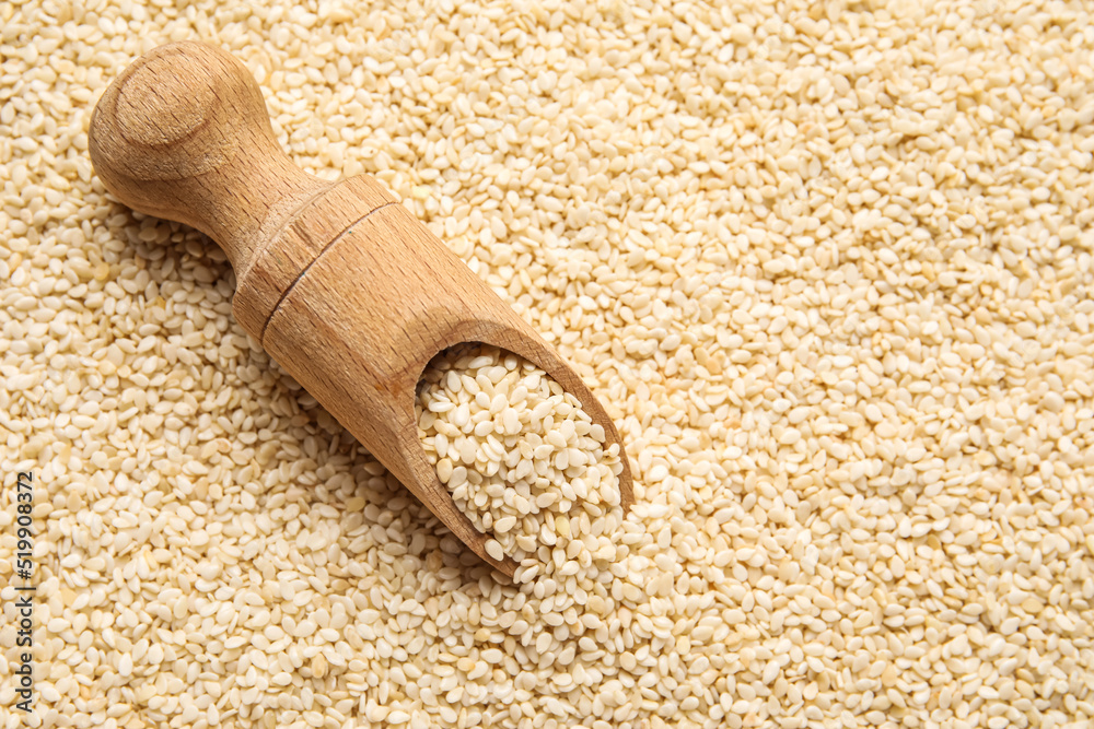 Wooden scoop with sesame seeds as background