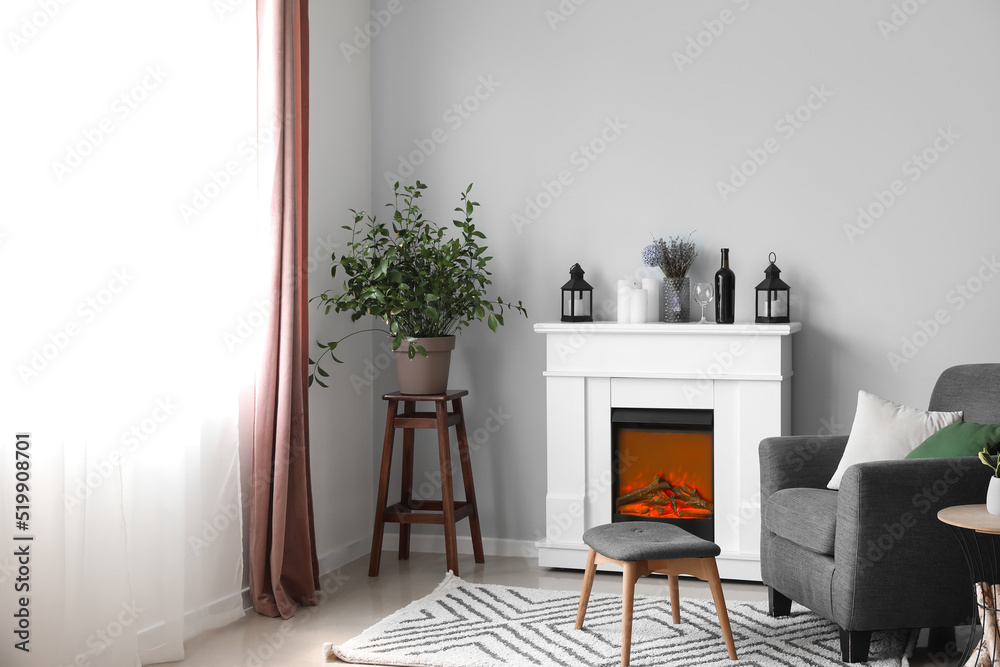 Interior of light living room with fireplace, candles and armchair