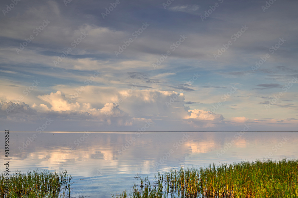 平静宁静的湖水美景，多云的天空倒影，坝上绿草如茵