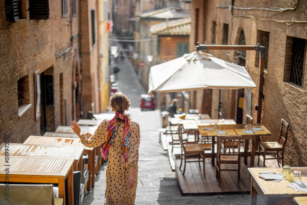 Sylish woman walks on narrow and cozy street in old town of Siena city. Concept of traveling in Tusc