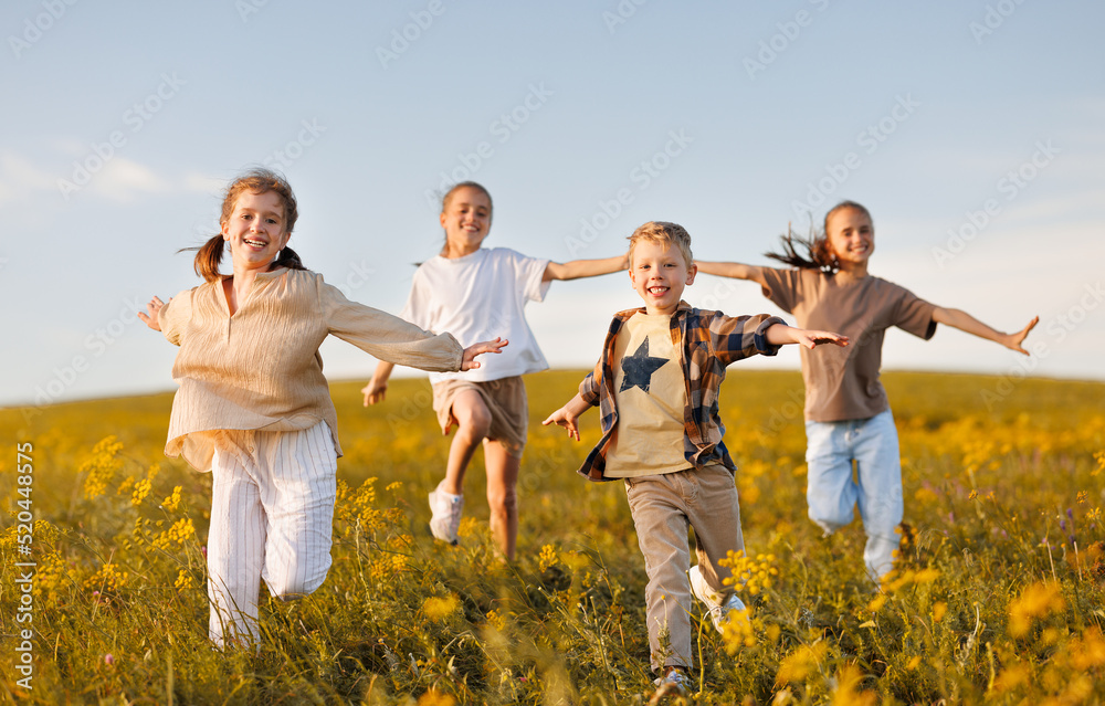 Group of happy joyful school kids   running with outstretched arms in field on sunny spring day, exc