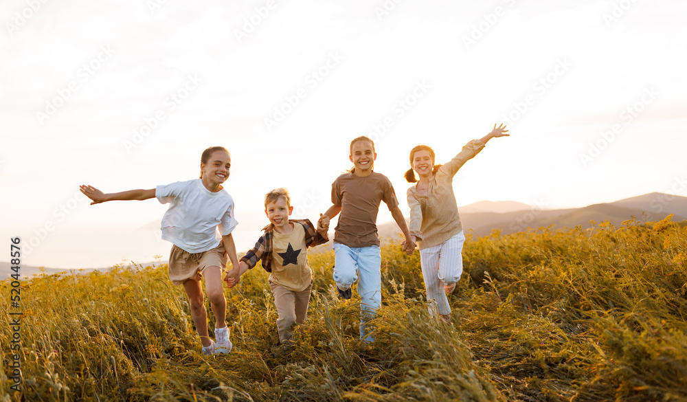 Group of happy joyful school kids boys and girls running with holding hands  in field on sunny day