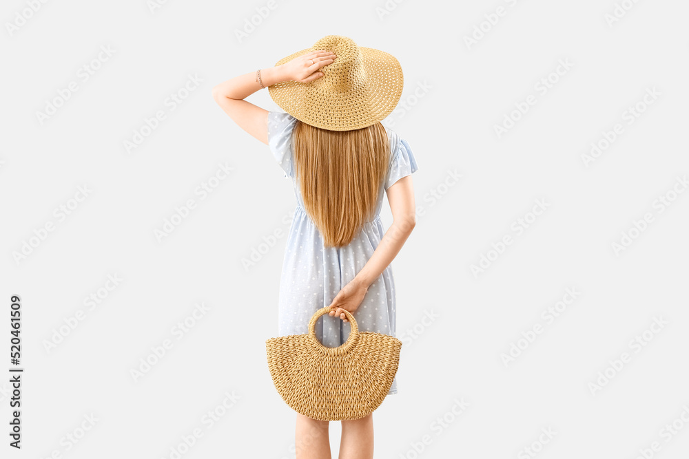 Young woman in wicker hat holding rattan handbag on light background