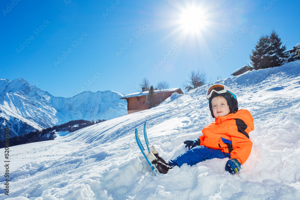 带着滑雪板的男孩准备去滑雪学校，坐在山上的雪地里