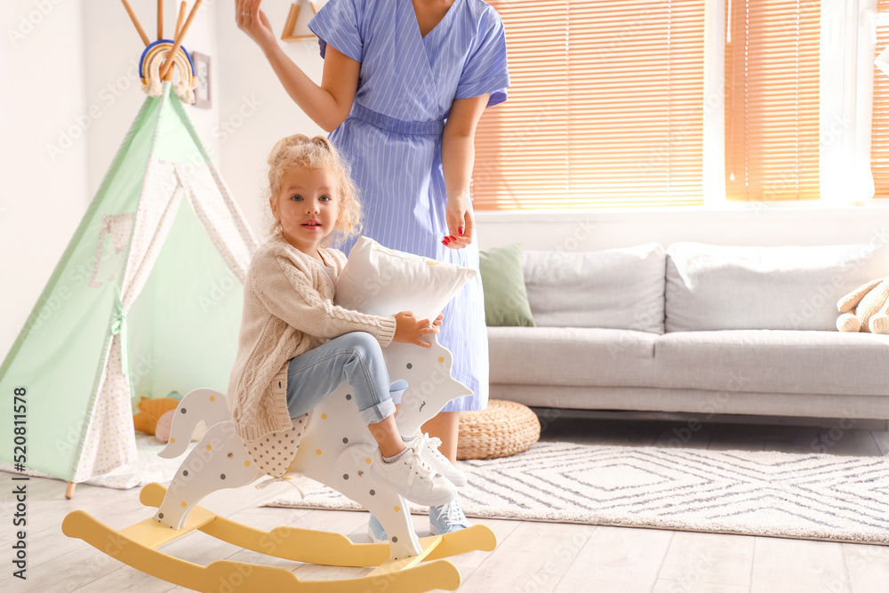 Cute little girl with pillow, rocking horse and her mother at home