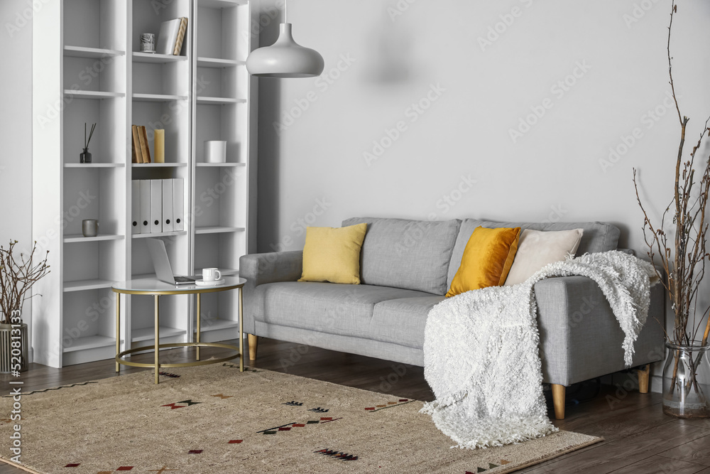 Interior of light living room with grey sofa, table and shelving unit