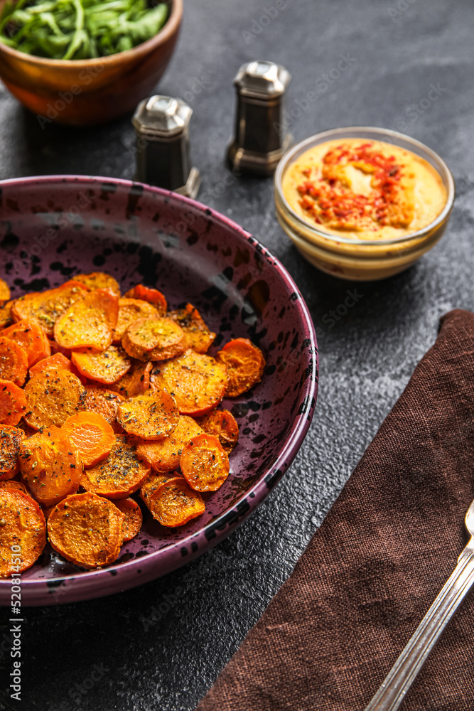 Bowl of tasty baked carrots on dark background, closeup