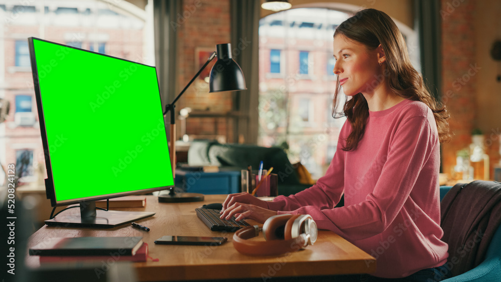 Young Pretty Female Working from Home on Desktop Computer with Green Screen Mock Up Display. Creativ