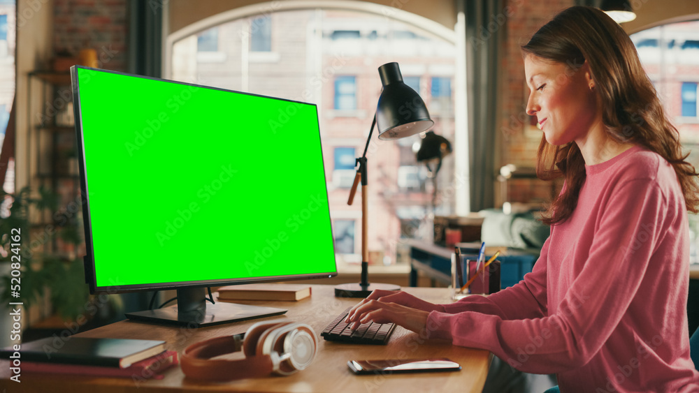 Young Beautiful Adult Woman Working from Home on Desktop Computer with Green Screen Mock Up Display.