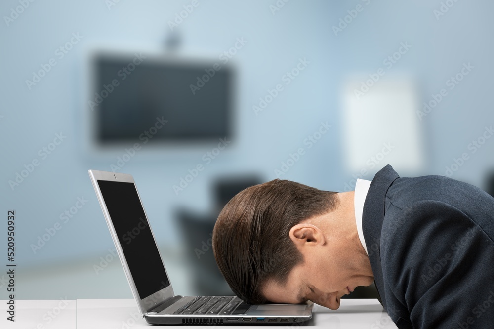 Tired exhausted man, office worker, manager or freelancer, sitting at his desk, tired of working in 