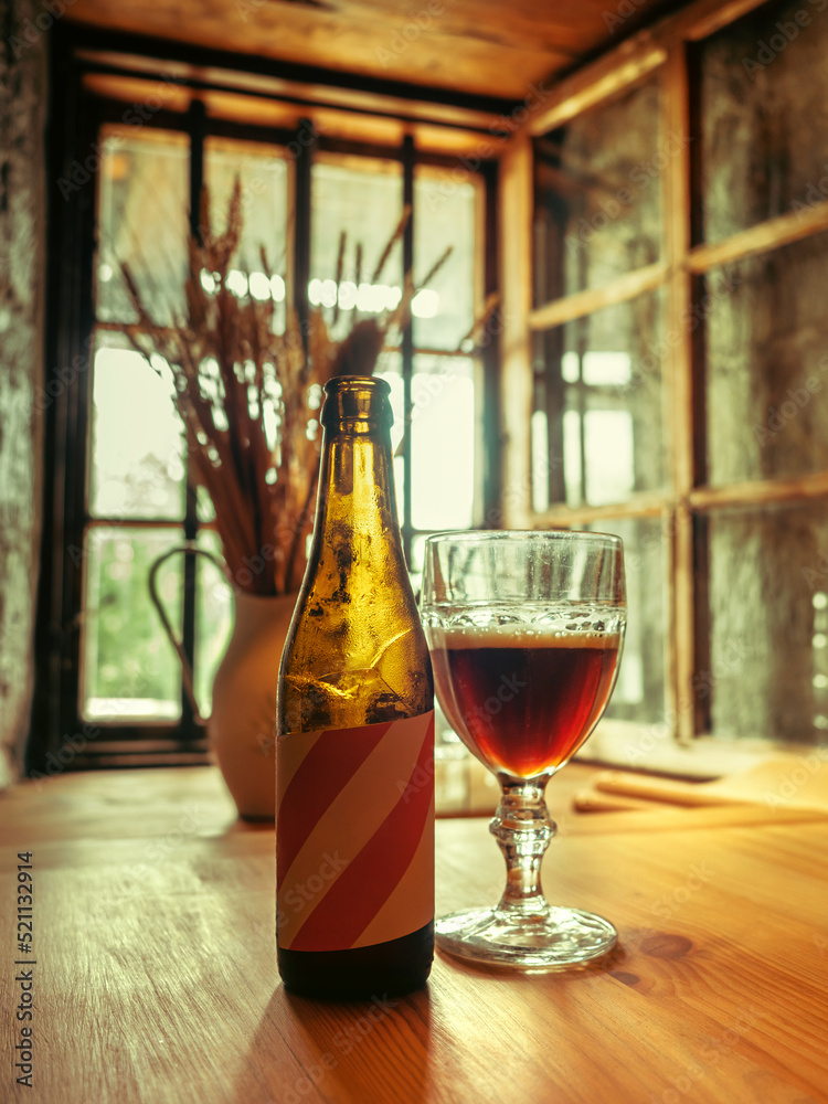 Glass bottle and glass filled with dark beer on a wooden table in a medieval castle