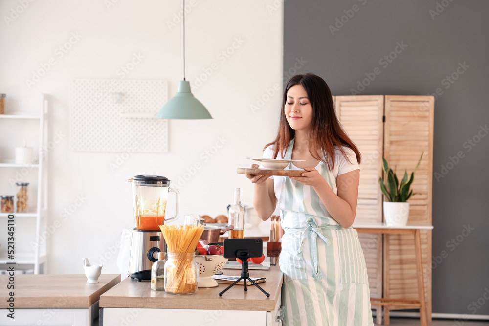 亚洲年轻女子在厨房观看烹饪视频教程后拿着南瓜汤的盘子