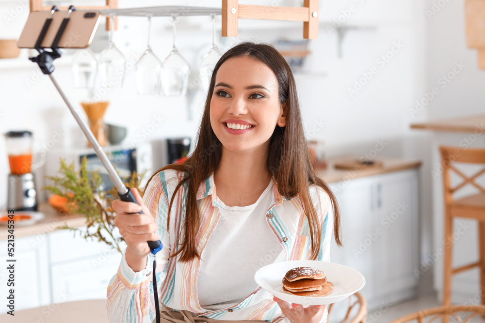 年轻女子拿着美味的煎饼在厨房自拍