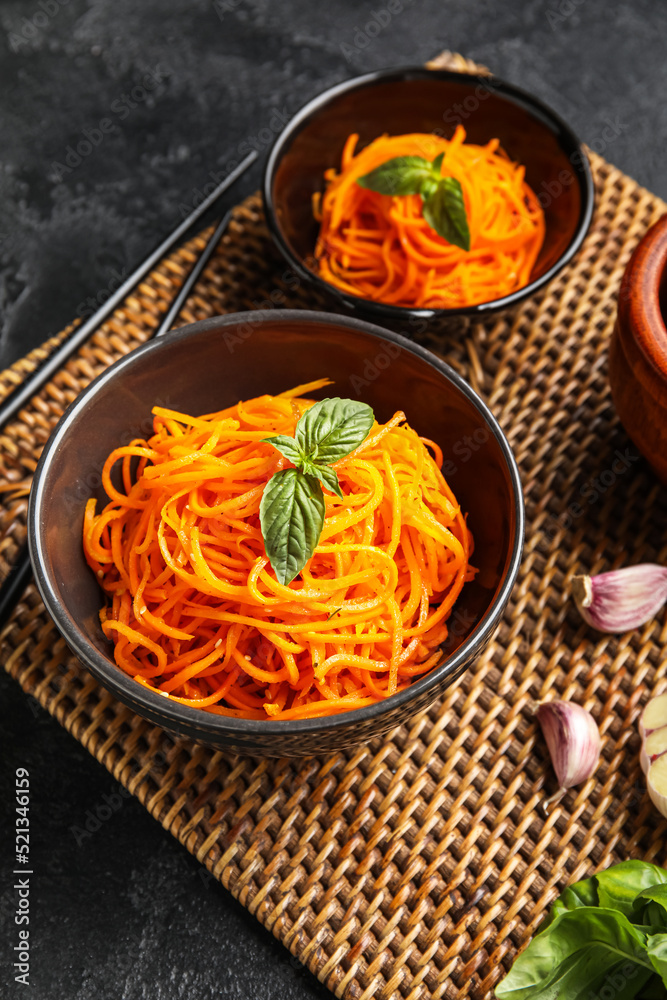 Bowls with spicy carrot salad on wicker mat