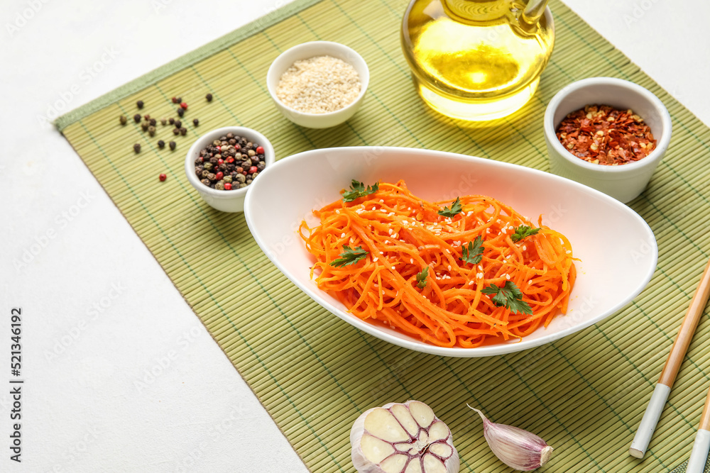 Bowl with spicy carrot salad and ingredients on white table