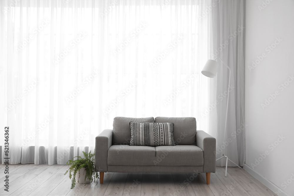 Interior of light living room with grey sofa, standard lamp and houseplant