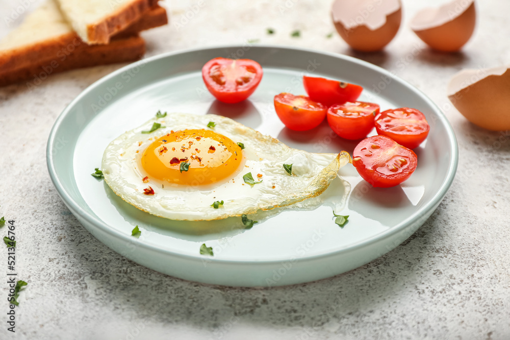 Plate with tasty fried egg and cut tomatoes on light background, closeup